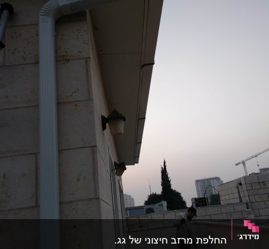 מרזב לבן מחובר לגג בניין אבן